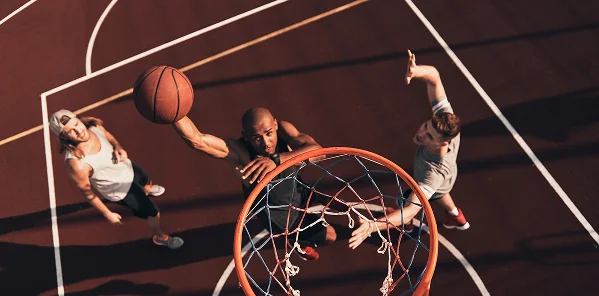 A imagem mostra um momento dinâmico de um jogo de basquetebol, onde um jogador realiza uma enterrada poderosa enquanto os adversários tentam detê-lo. O quadro transmite a tensão do jogo, a velocidade, as emoções e o verdadeiro dinamismo do basquetebol de rua.